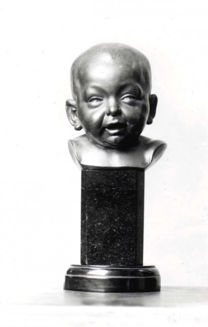 Black and white image of a bronze sculpture of an infant's head on a marble platform.