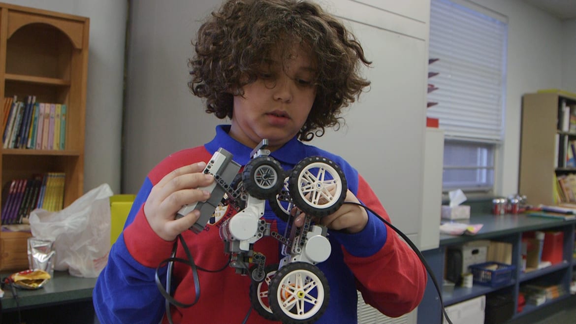 Young boy holding up electrical device with wheels.