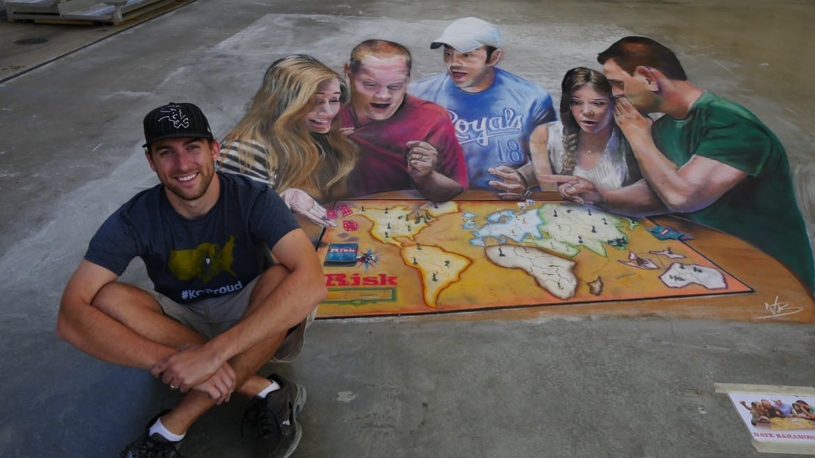 Artist Nate Baronowski sits in front of his Risk-themed chalk rendering.