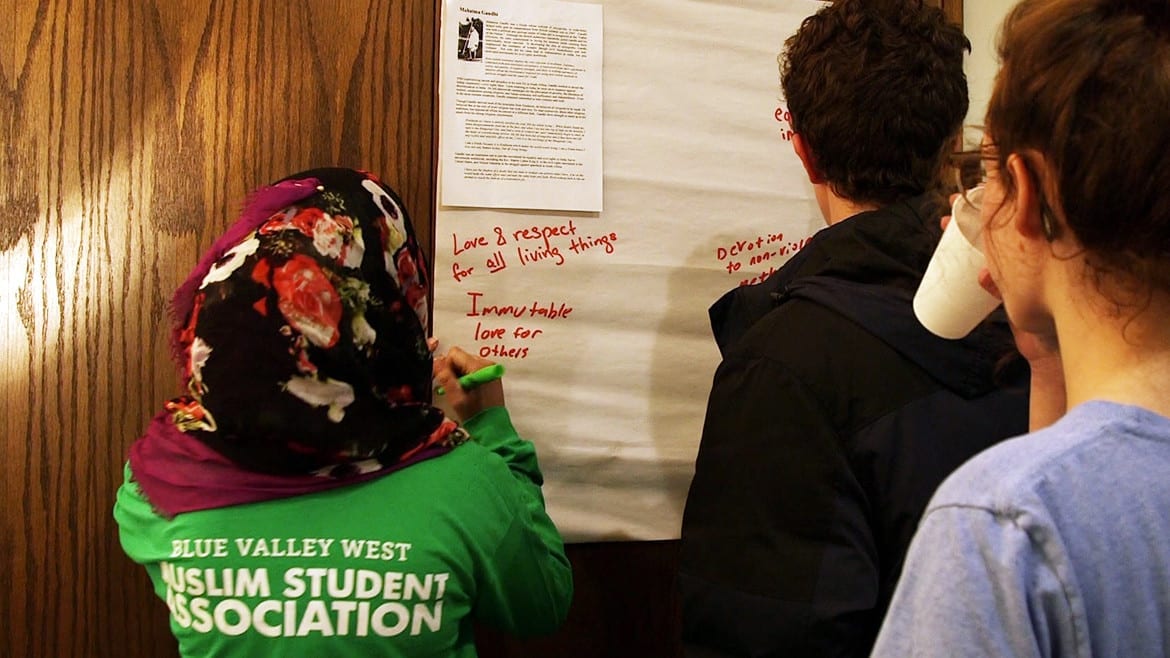 Young woman in green shirt writes on paper.