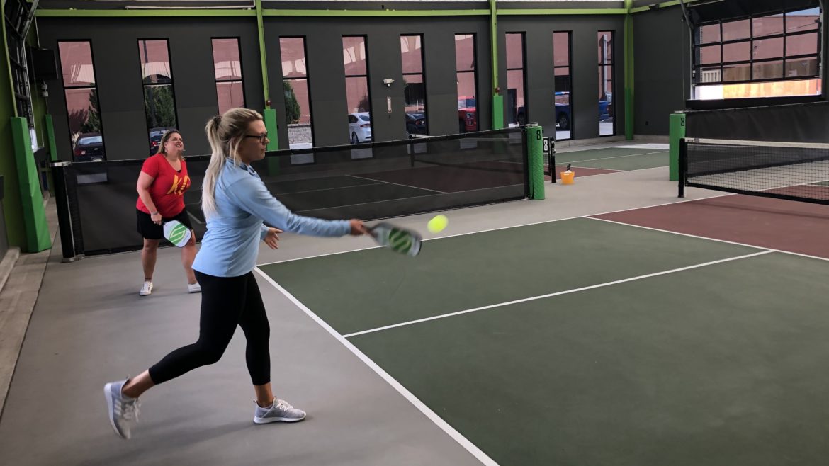 A woman serves the ball in a pickleball match.