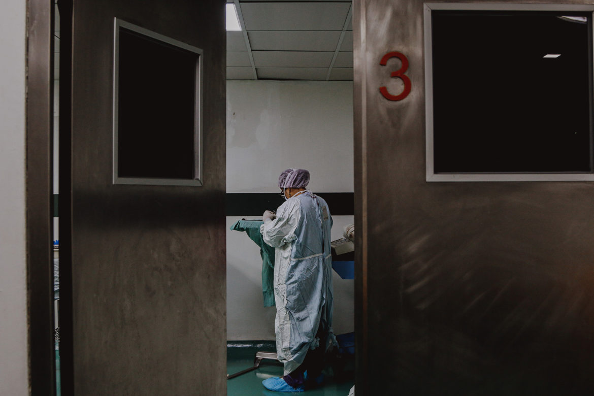 A photo frames a hospital hallway, as a health care worker in their gown looks down with their back facing the camera. This image accompanies the Flatland guide on what to know about the evolving standards of care in hospital systems and health care clinics.