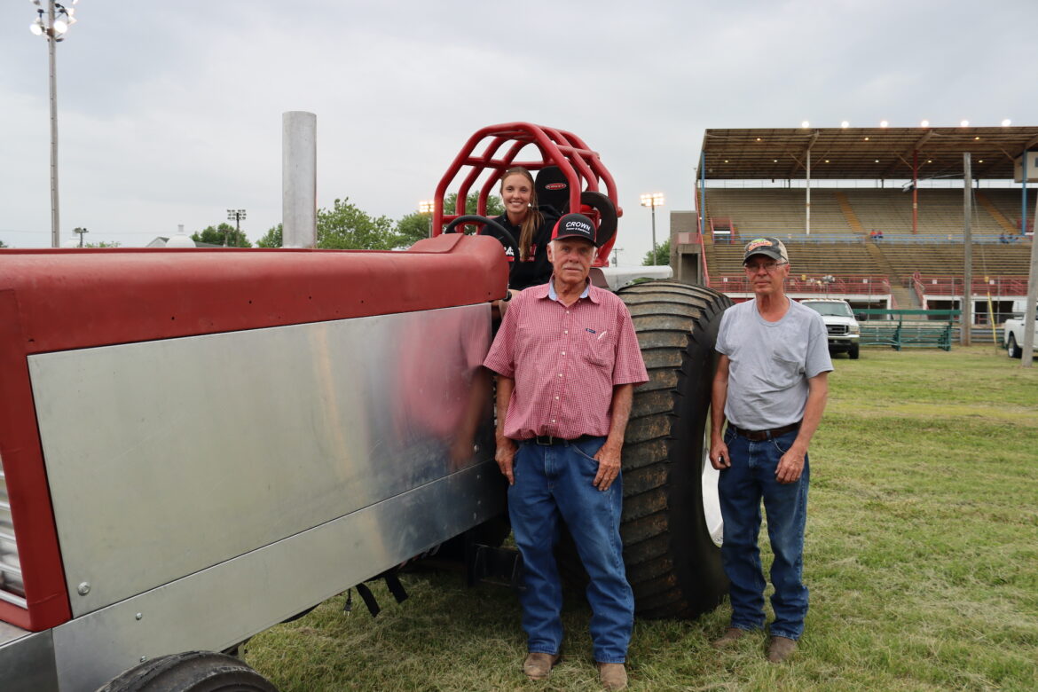 Woman sits on a tractor while and older man and a middle aged man stand to the side.