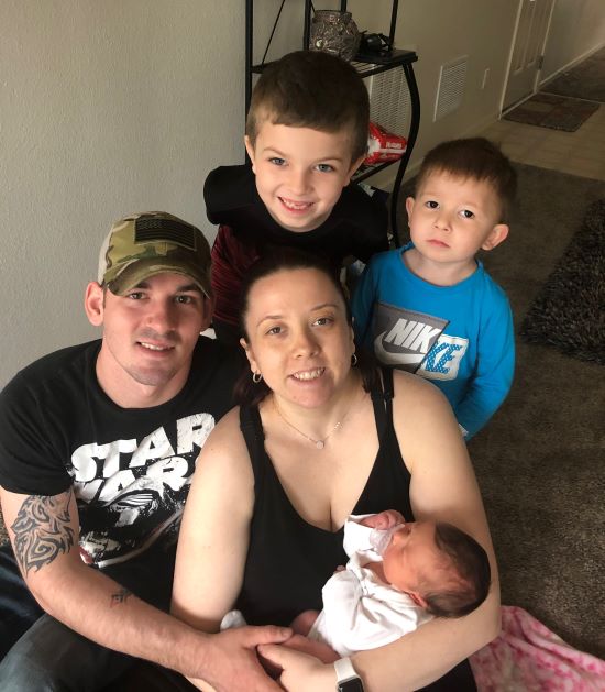 Woman holds baby next to her husband and two young boys.