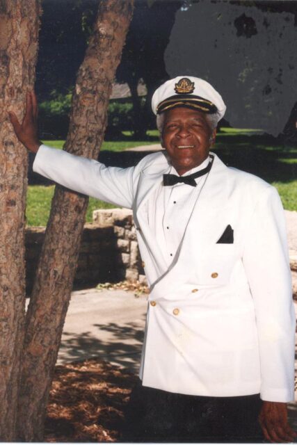Eddie Baker, a well-known Kansas City musician, stands by a tree in a white coat and bowtie. Baker was responsible for opening the Charlie Parker Memorial Foundation.