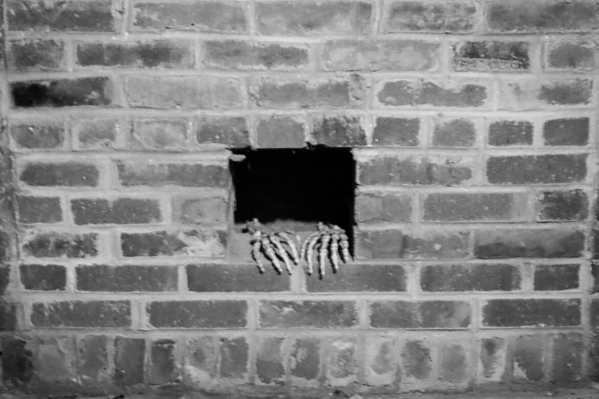 skeleton hands stick out of a hole in a brick wall.
