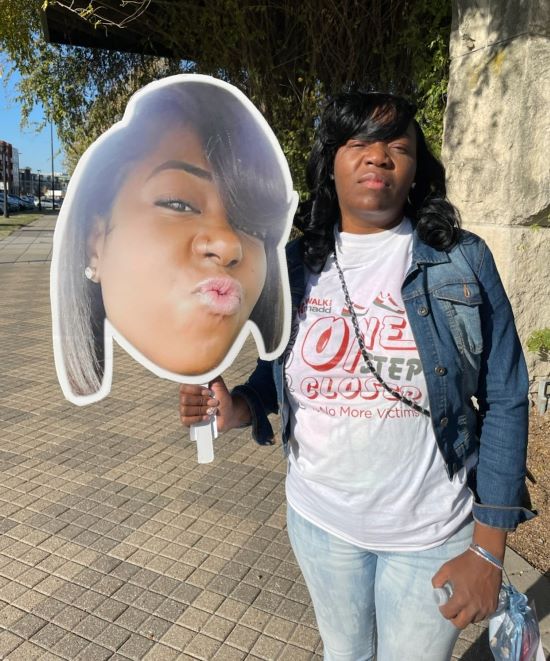 Kizzy Dickerson holding a handheld poster of her daughter, Ty'ana Bryant, who died in a car crash in 2018.