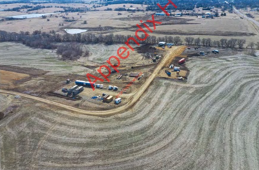 Aerial photo of a field with some shipping containers, cars and a dirt road.