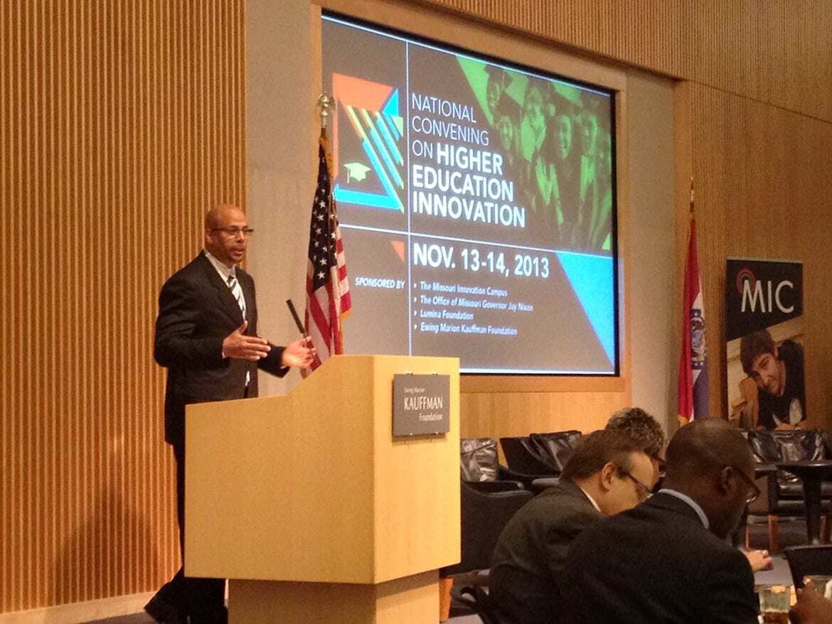 Man in suit and tie standing at podium in front of screen that reads "National Convening on Higher Education Innovation"