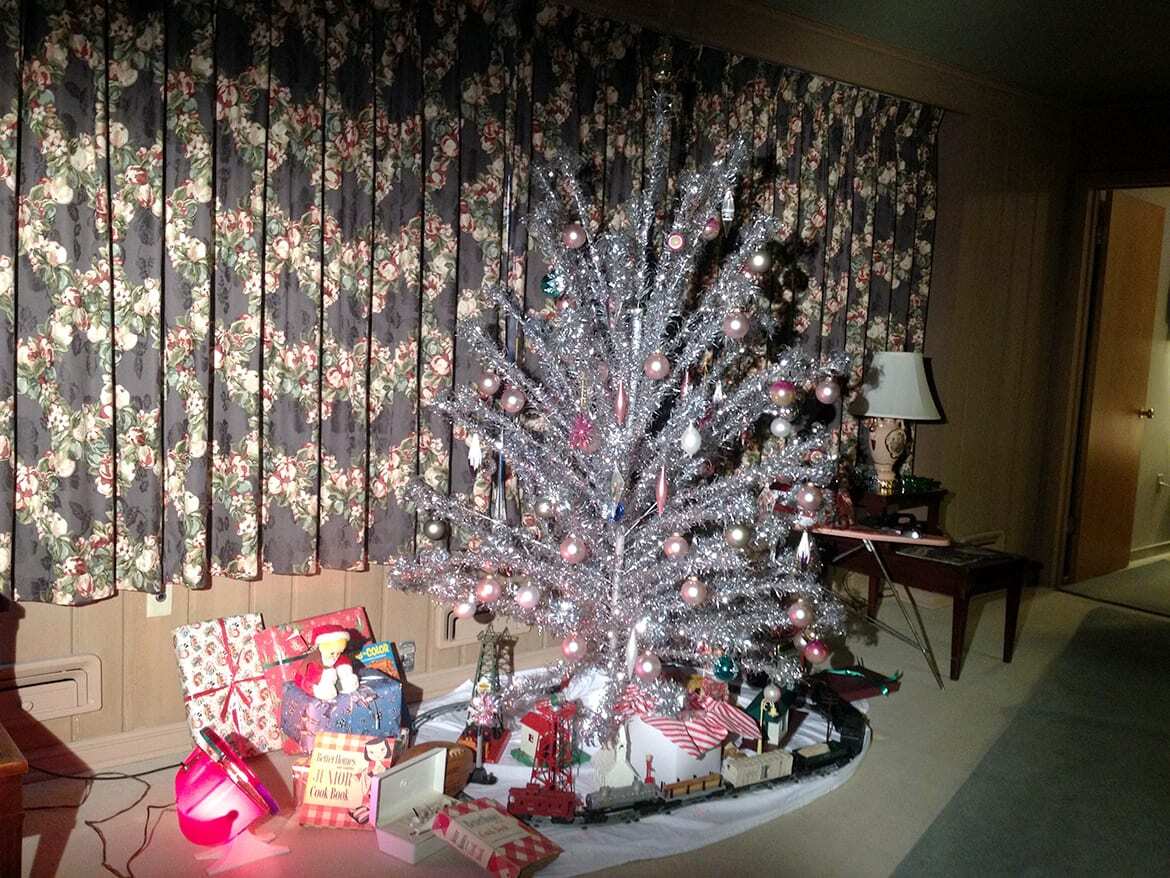 Aluminum Christmas Tree illuminated by a rotating color-wheel in 1950s looking living room with 1950s era present under the tree.