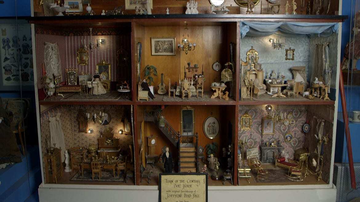 Wide image of Victorian dollhouse with three stories and seven ornately furnished rooms.