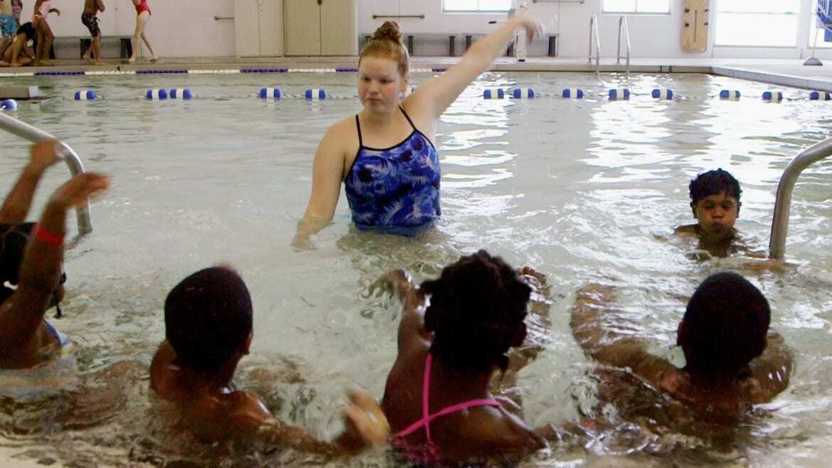 Woman teaching students to swim in pool.