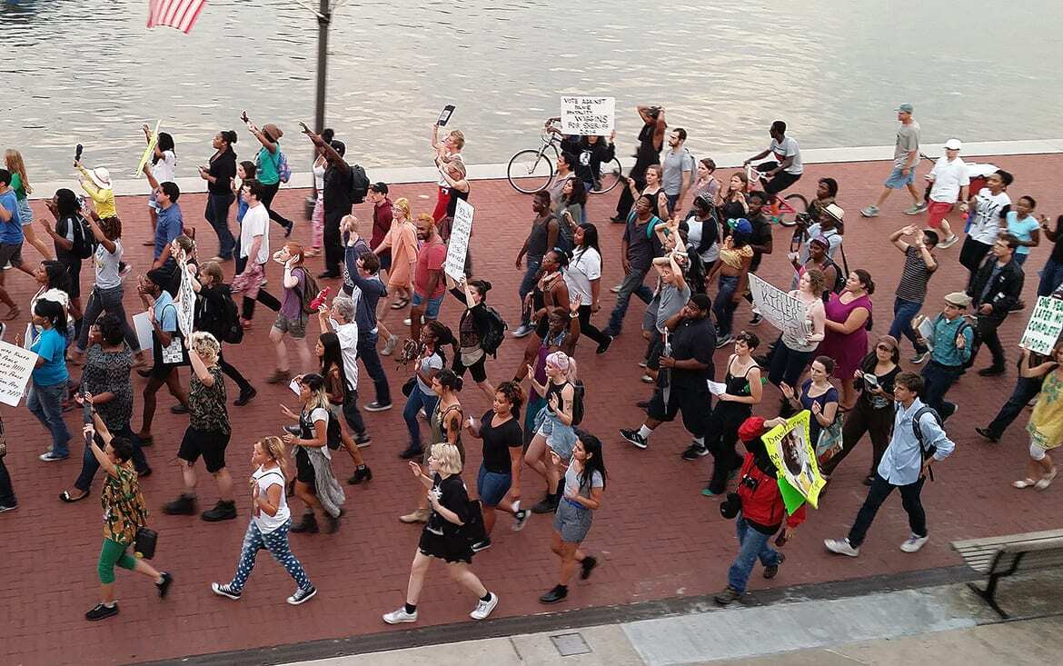 Photo of people marching in the streets, many with their hands up.