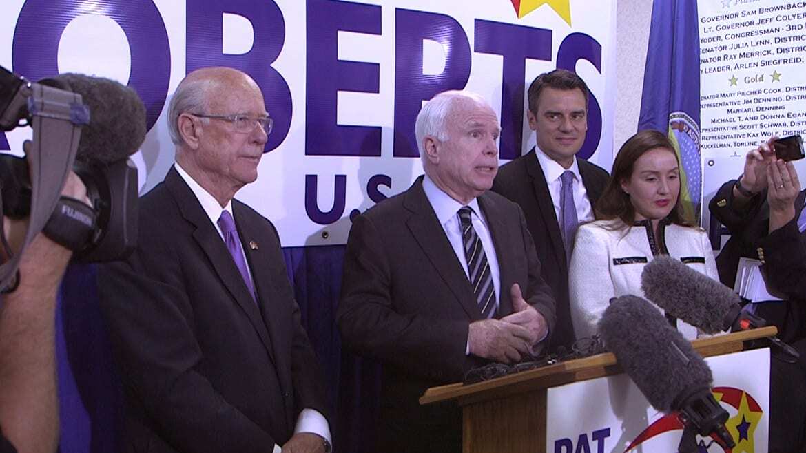 Photo of Pat Roberts, John McCain, Kevin Yoder and Yoder's wife standing behind a podium surrounded by cameras.
