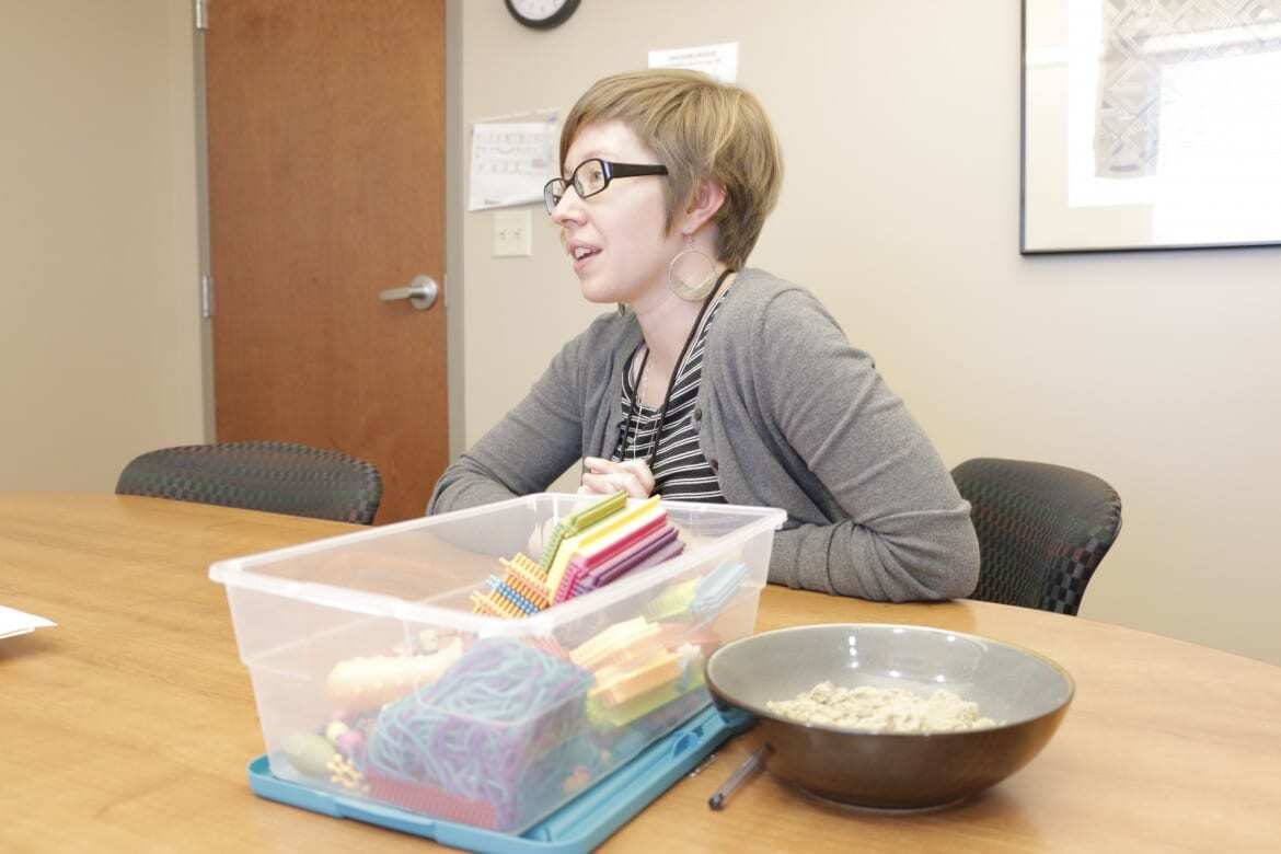 A woman sits at a conference table next to small building blocks and a bowl of sensory sand.