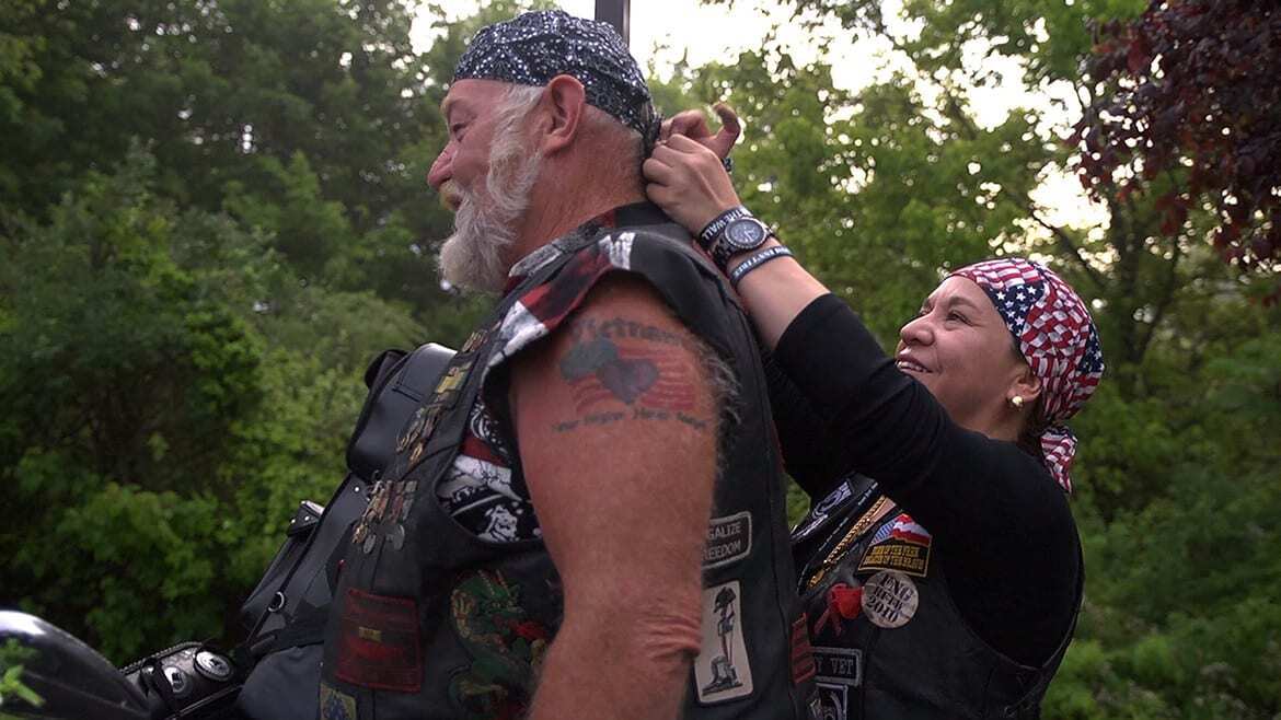 Woman ties bandana on man's head.