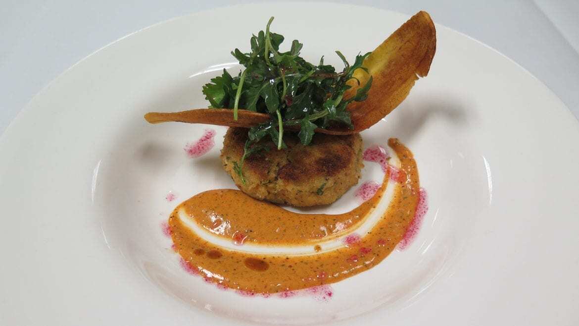 A crab cake with a chip and sauce.