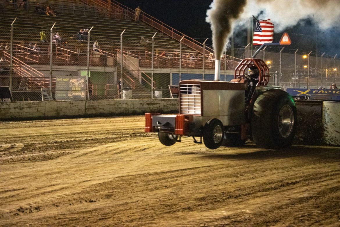 A tractor spews mud up as it drags a weighted sled across the mud.