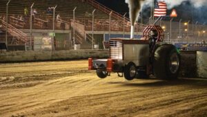 A tractor spews mud up as it drags a weighted sled across the mud.