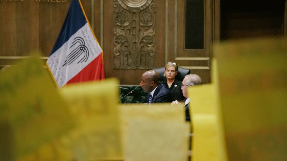 Mayor Quinton Lucas speaks at the Aug. 17 committee meeting, behind yellow KC Tenants protest signs. At least eight KC Tenants leaders gave testimony at this meeting, and dozens of members returned the next day for the City Council vote.