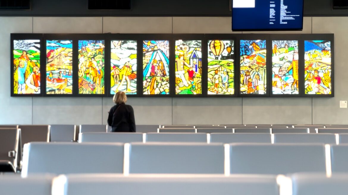 View from rows of seats to person viewing horizontal row of backlit stained glass panels.