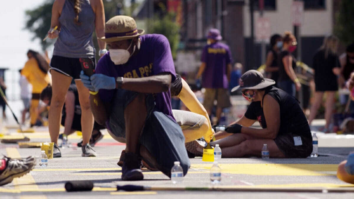 Man in hat and mask squats working on Black Lives Matter street in Kansas City.
