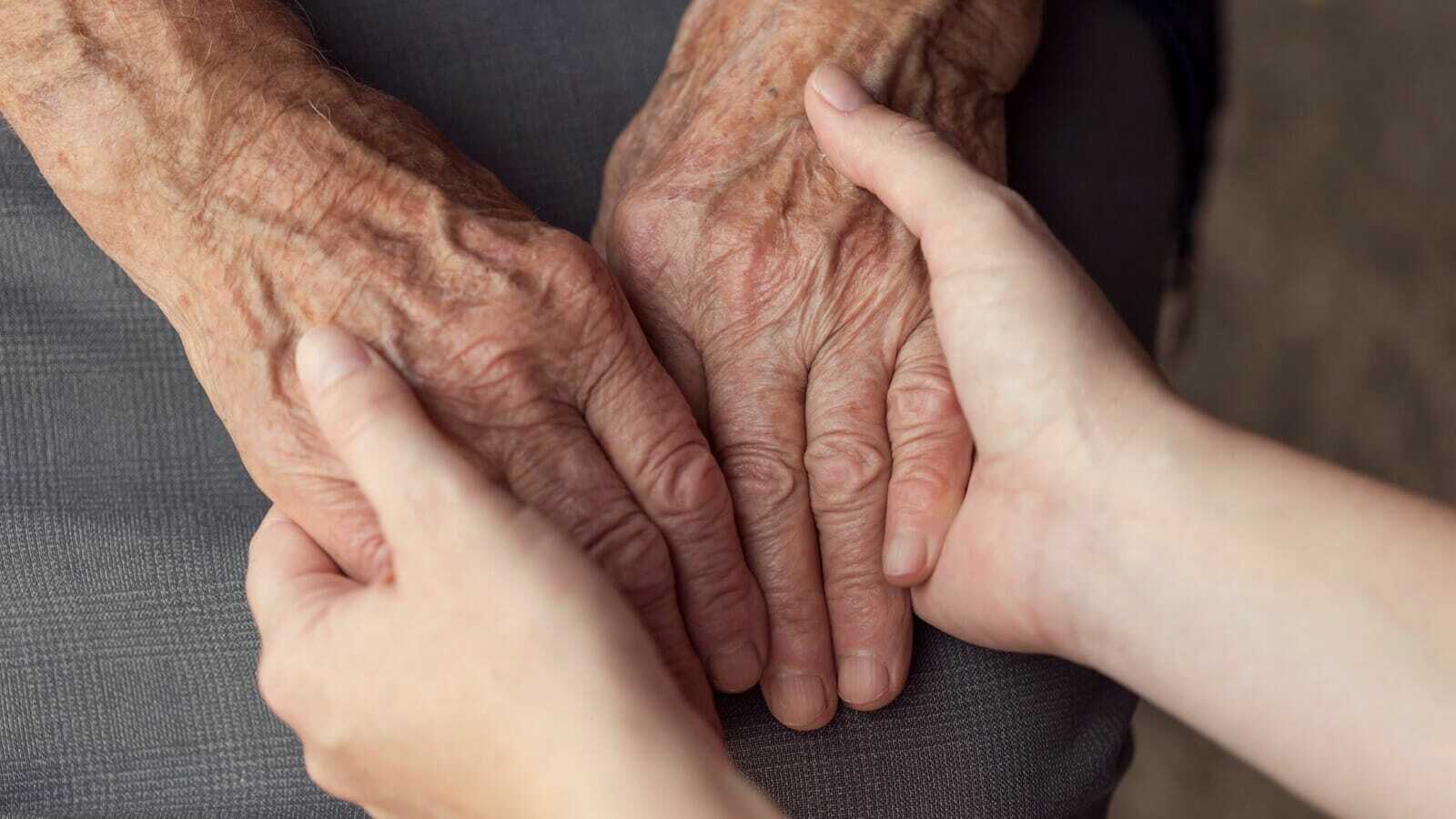 An older adult and a younger person holding hands as they consider long-term care options.