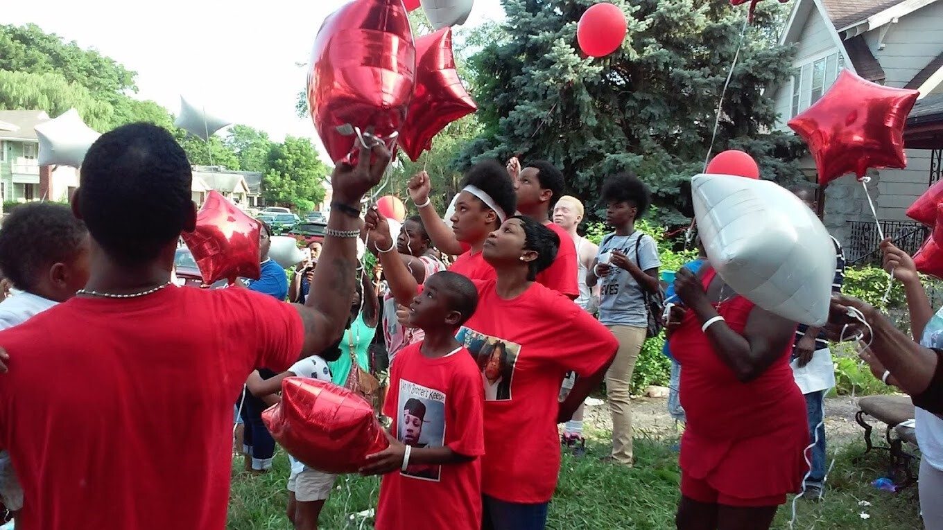 crowd of people in red t-shirts with red balloons at a memorial vigil.