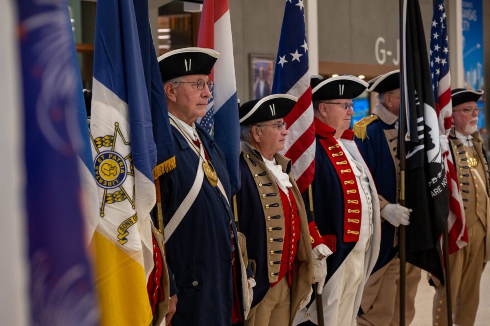 From left, Alan Martin of Shawnee, Kansas, Michael Robertson of Platte City, Missouri, and Jeff Winters of Olathe, Kansas, wait at the Kansas City International Airport on Veterans Day 2025 for the return of veterans who traveled to Washington, D.C. on an Honor Flight. They are members of the Sons of the American Revolution Color Guard. (Todd Feeback | Flatland)