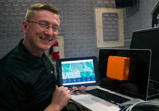 Heath Gerlock, a founder of Farmobile, shows the orange box device that can feed farm data directly to a tablet, smartphone or computer. Gerlock pictured in the Iowa Public Radio studio in Ames. (Amy Mayer/Harvest Public Media)