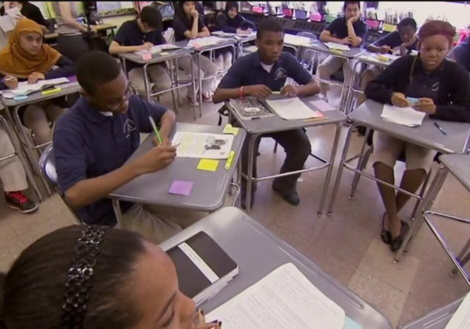 Students sit at desks in a circle and discuss assignment.