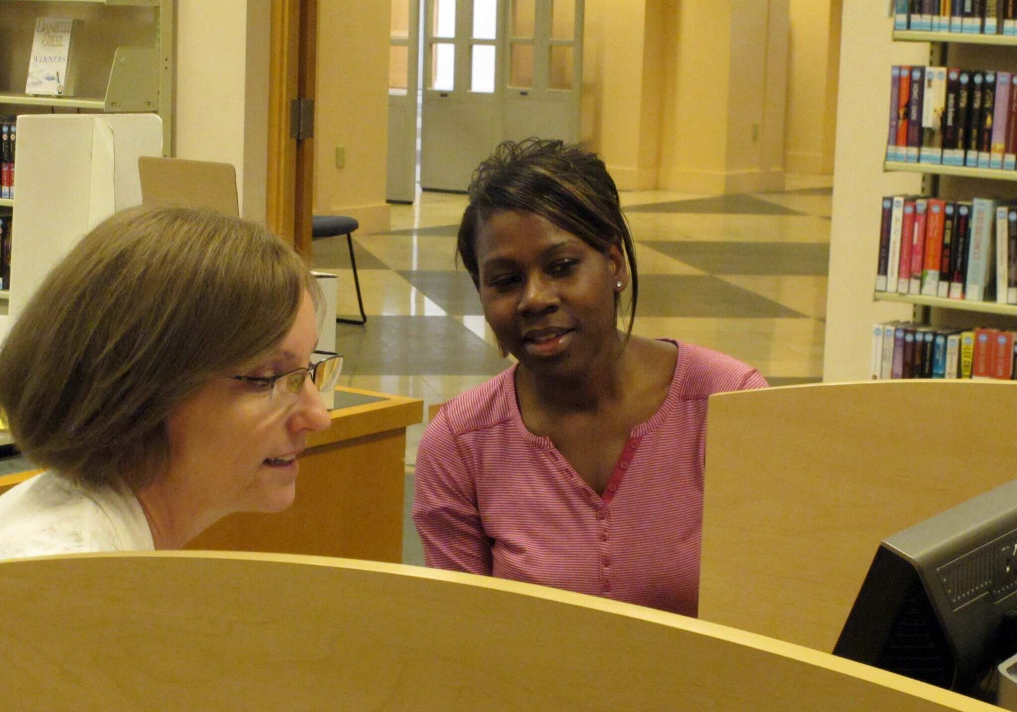 In this photo from Monday, March 31, 2014, Teresa Holmer, left, a health care navigator for the Shawnee County, Kan., Health Agency, counsels Topeka resident Tamika Terry about obtaining insurance coverage at the public library in Topeka, Kan. About 57,000 Kansas residents enrolled in health plans through the federal government's online health insurance marketplace. (AP Photo/John Hanna)