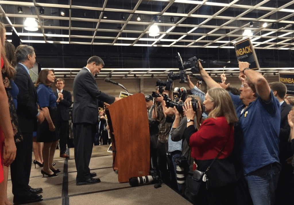 Photo of Sam Brownback at podium addressing crowd