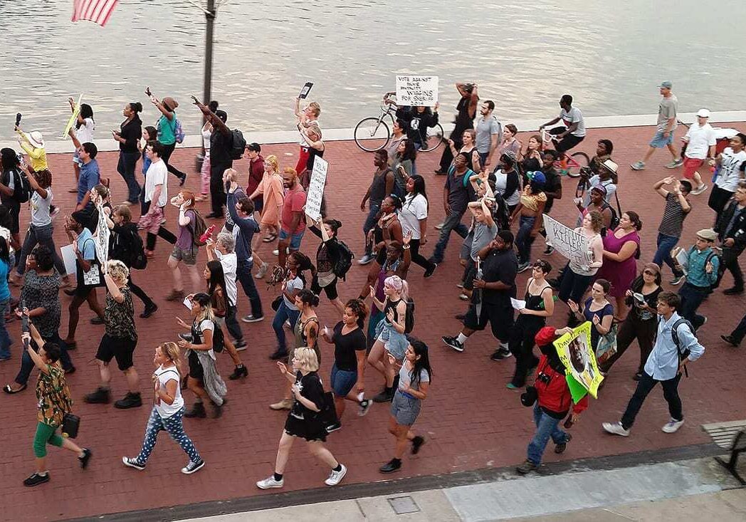 Photo of people marching in the streets, many with their hands up.