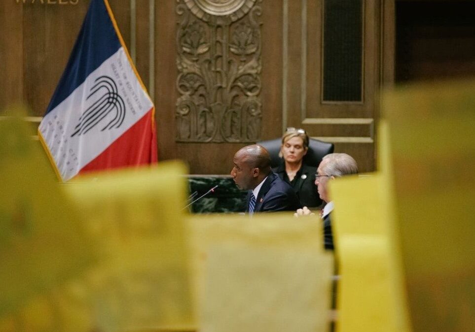 Mayor Quinton Lucas speaks at the Aug. 17 committee meeting, behind yellow KC Tenants protest signs. At least eight KC Tenants leaders gave testimony at this meeting, and dozens of members returned the next day for the City Council vote.