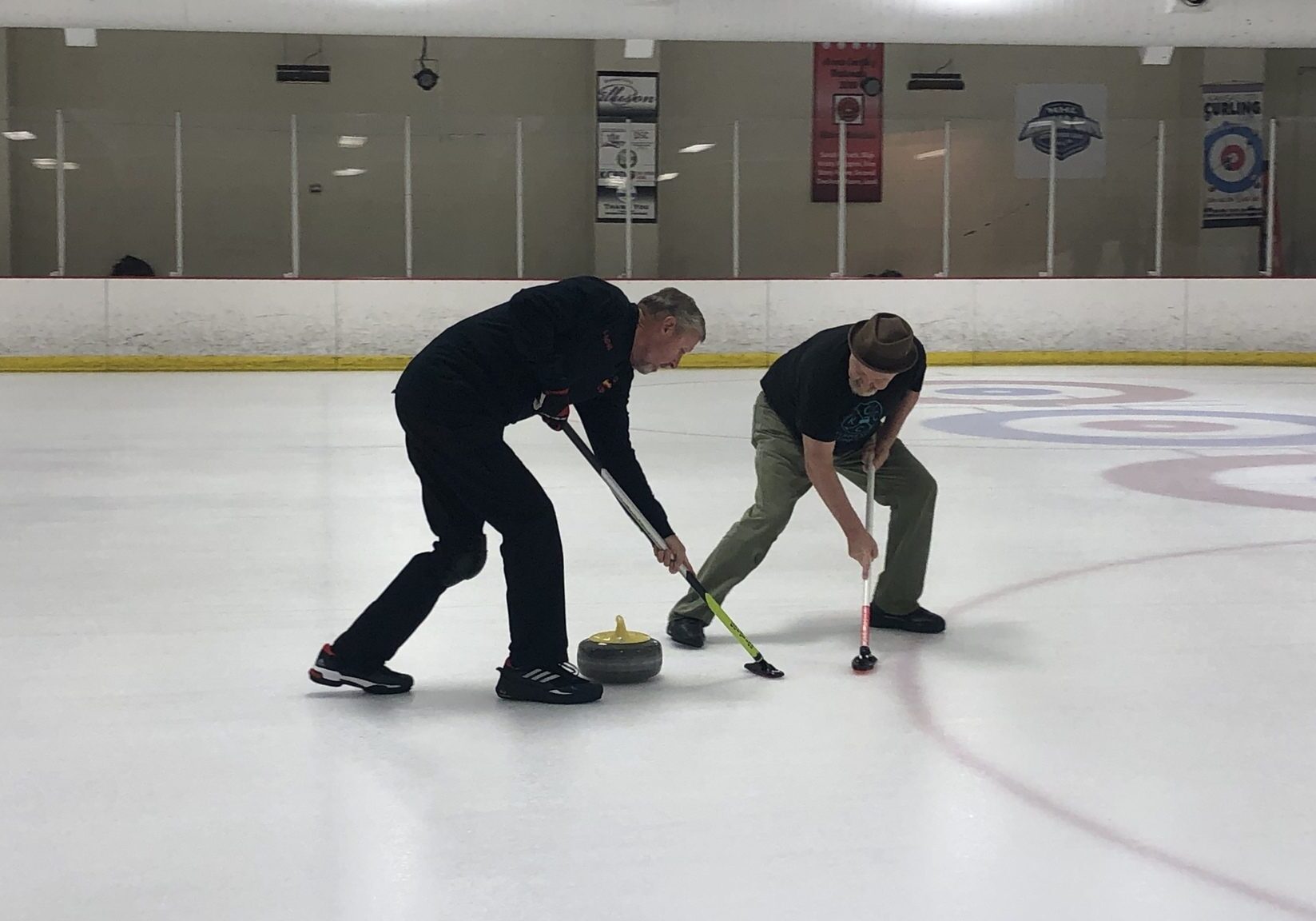 A pair of curlers sweep in front of the stone.