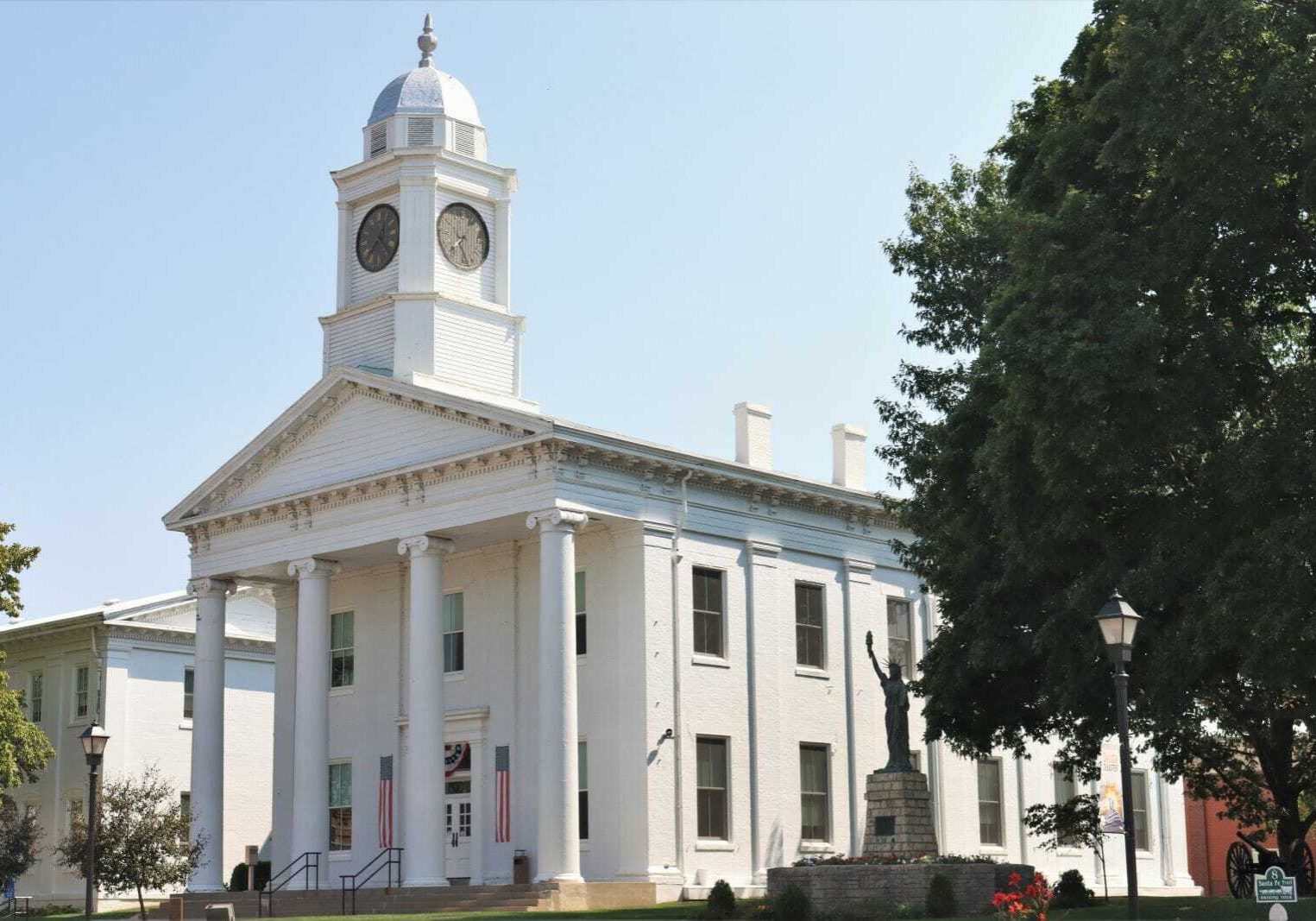 A white courthouse built in the Greek revival style. On top the building is a clock tower.