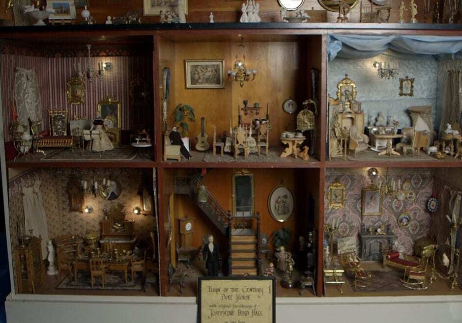 Wide image of Victorian dollhouse with three stories and seven ornately furnished rooms.