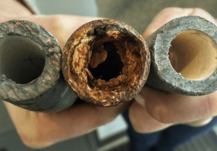 An individual holds a lead pipe, a steel pipe and a lead pipe treated with protective orthophosphate.