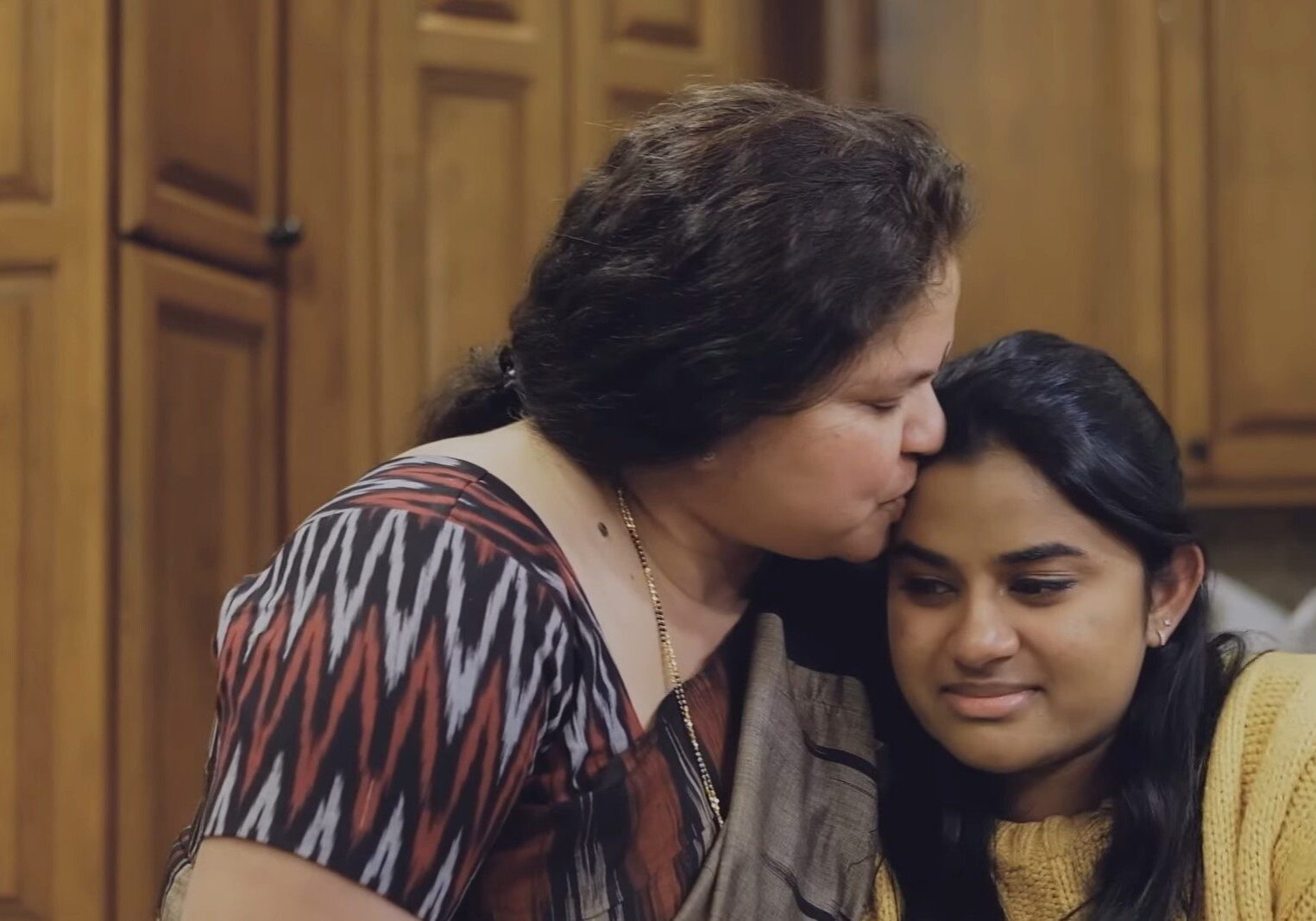 A mother kisses her daughter on the forehead. The daughter is crying,