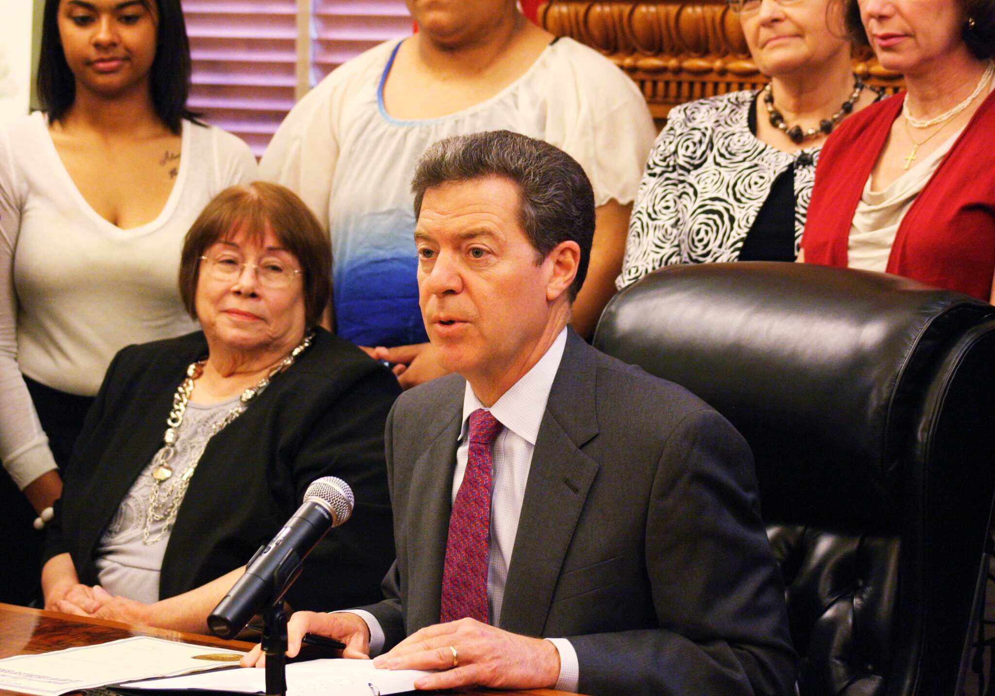 Phyllis Gilmore, secretary of the Kansas Department for Children and Family Services, listens to Gov. Sam Brownback make remarks about foster care services during a ceremony Monday, May 13, 2013, in Topeka, Kan. Gilmore says some 5,600 children are in the Kansas foster care system and that more foster parents are needed to meet demand. (AP Photo/John Milburn)