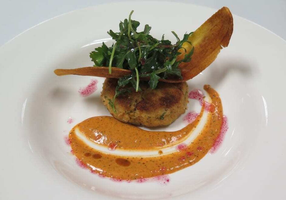 A crab cake with a chip and sauce.