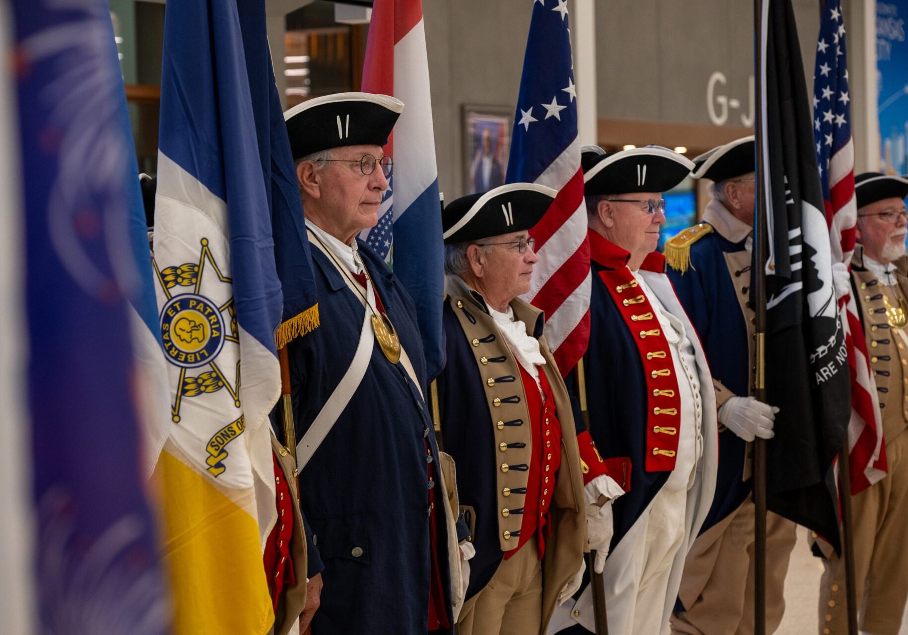 From left, Alan Martin of Shawnee, Kansas, Michael Robertson of Platte City, Missouri, and Jeff Winters of Olathe, Kansas, wait at the Kansas City International Airport on Veterans Day 2025 for the return of veterans who traveled to Washington, D.C. on an Honor Flight. They are members of the Sons of the American Revolution Color Guard. (Todd Feeback | Flatland)