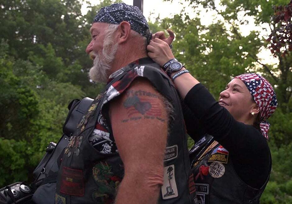 Woman ties bandana on man's head.